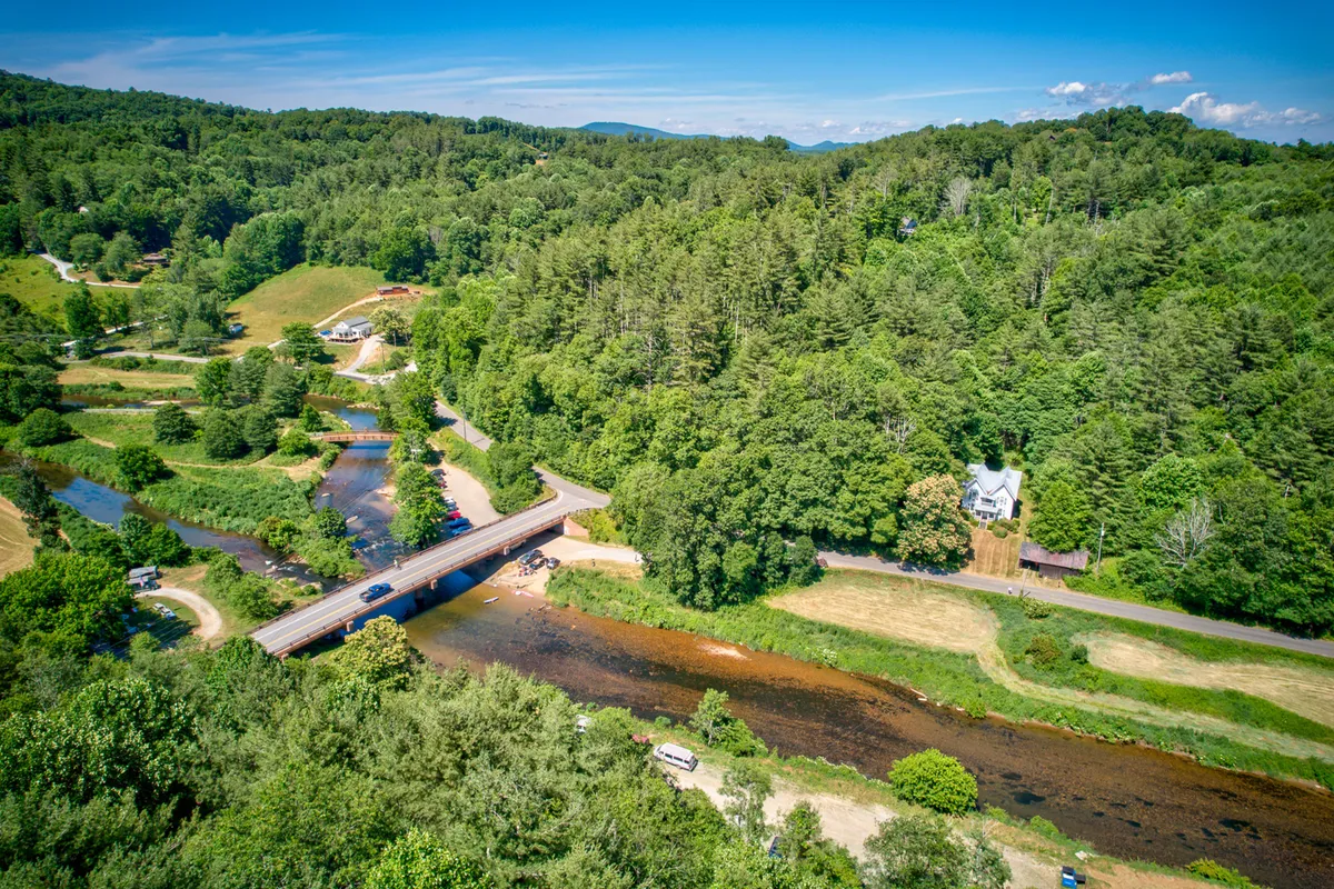 This image features a serene view of a river winding through wooded hills, crossed by a charming bridge and dotted with houses. The scene is tranquil and offers a sense of connection with nature, perfect for those seeking a peaceful backdrop for remote work.