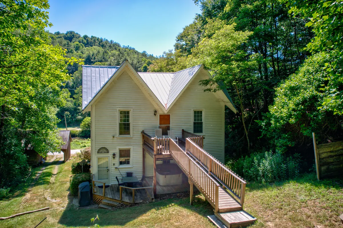 The house's unique front porch and distinctive gable roof are framed by surrounding trees and greenery, creating a peaceful and welcoming entrance. The inviting porch offers a serene place to relax and connect with the home's story and the surrounding environment.