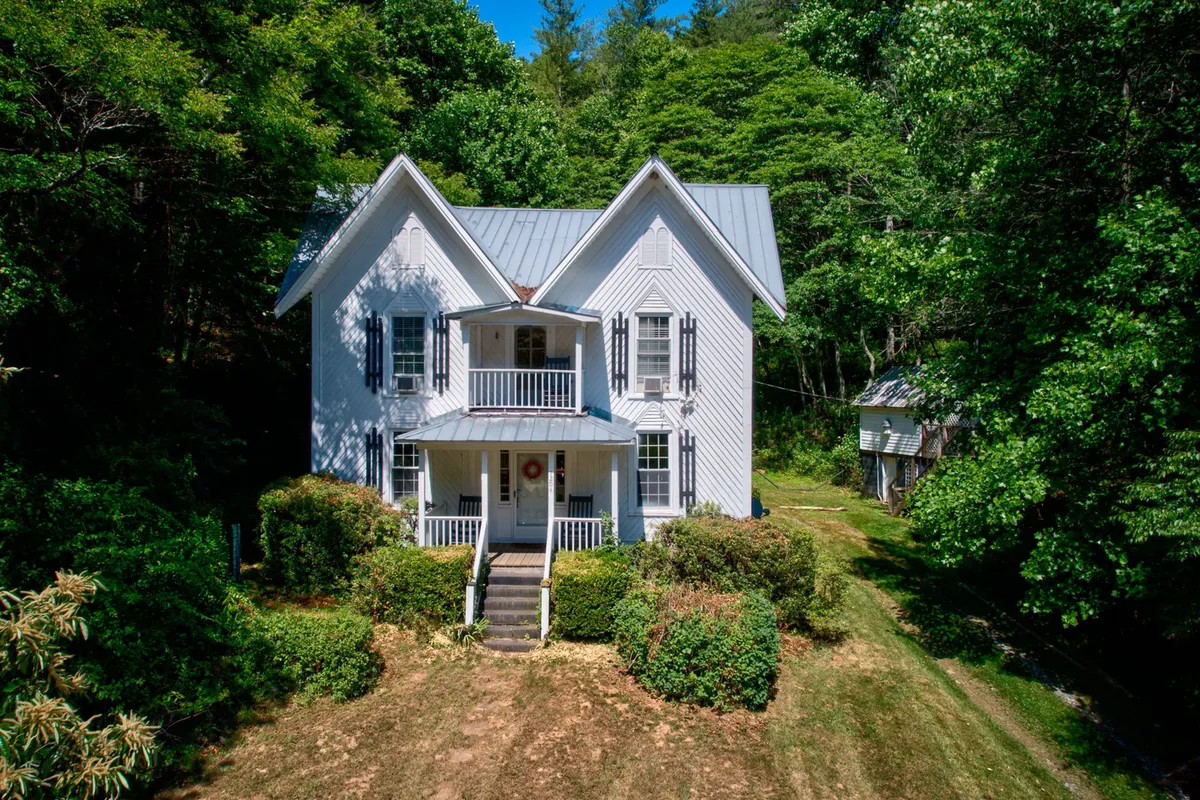 A view of the historic home with its inviting front porch, surrounded by landscaped gardens. The porch features comfortable seating, ideal for relaxing or socializing, while the garden offers space for kids to play and for families to gather.