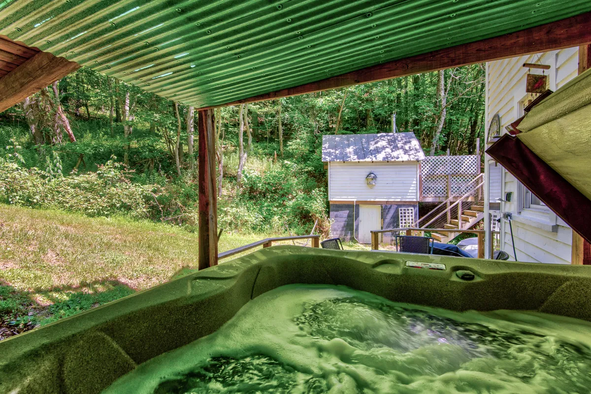 An exterior shot focusing on a hot tub set against lush greenery and with a shed in the background. The outdoor amenities are visible, hinting at opportunities to relax after outdoor adventures.