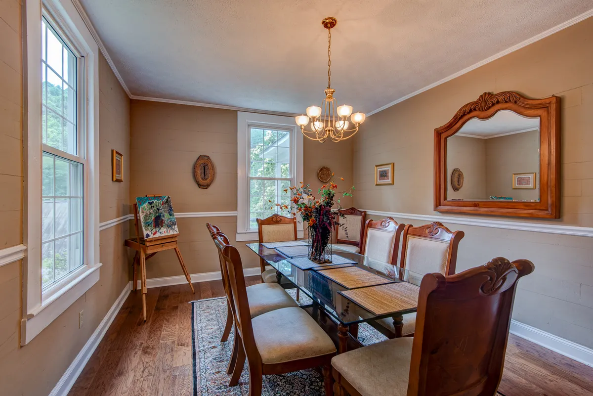 A warmly lit dining space featuring a substantial dining table with a flower arrangement and a chandelier. The nearby mirror reflects the natural light, amplifying the welcoming mood—ideal for sharing stories, celebrating special moments, and enjoying meals together.