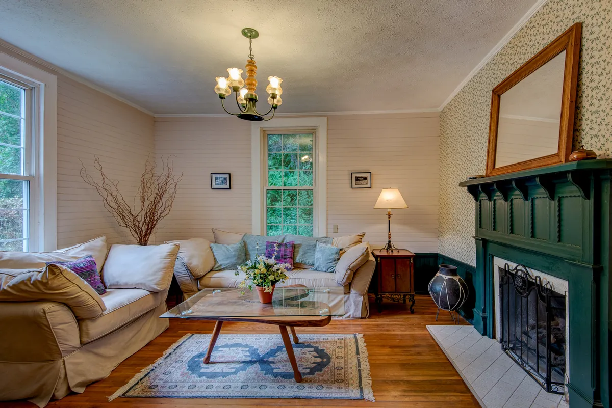 A welcoming living room with a plush comfortable sofa, an inviting fireplace, a coffee table topped with fresh flowers, and a sparkling chandelier above. Sunlight streams in, highlighting the warmth and comfort of the space, perfect for relaxing after a day of adventure or gathering for conversation.