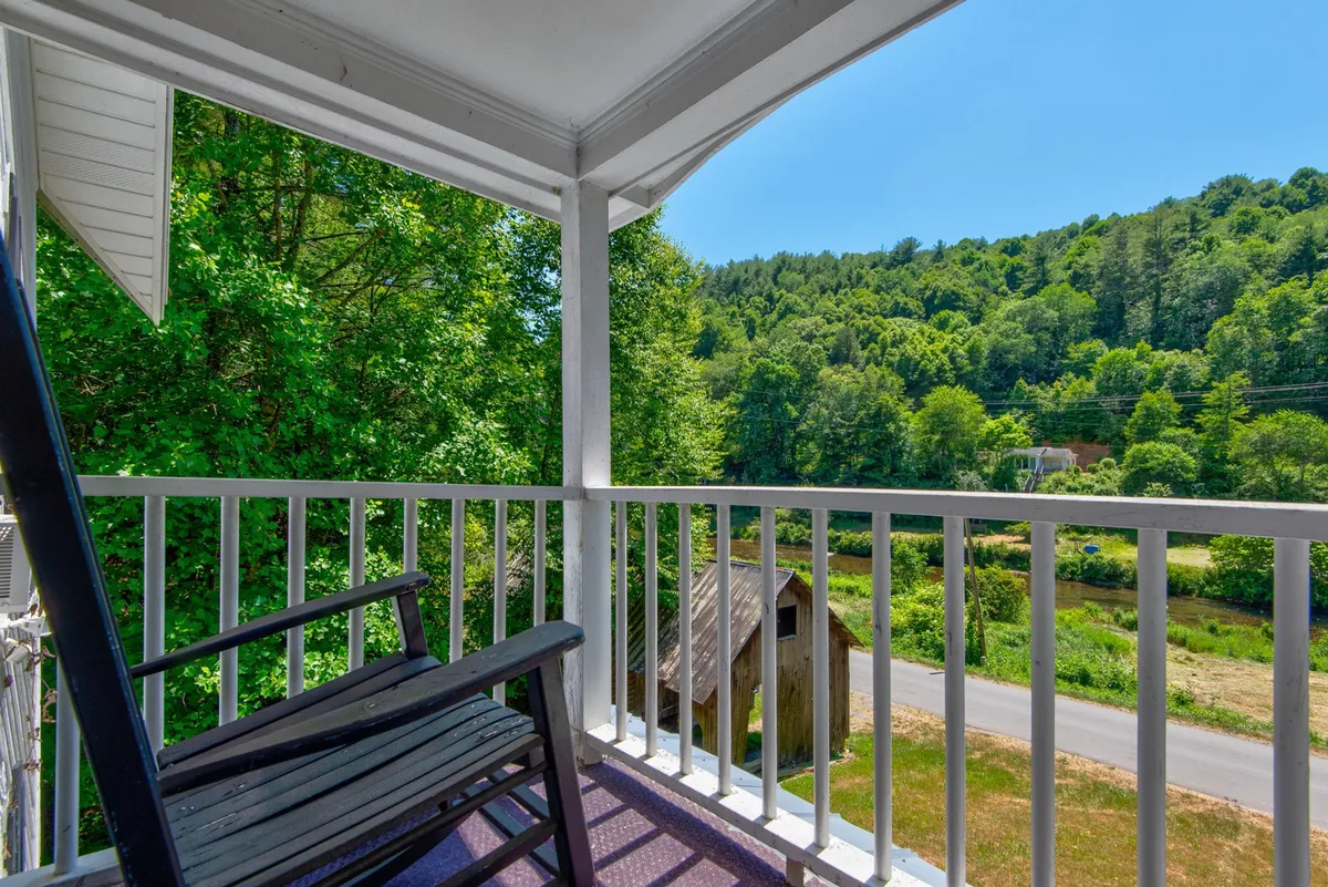 A cozy exterior scene with a classic rocking chair on the porch, overlooking lush greenery and distant hills. The setting suggests peaceful moments spent reading, sipping coffee, or reflecting on the area's scenic beauty and quiet history.