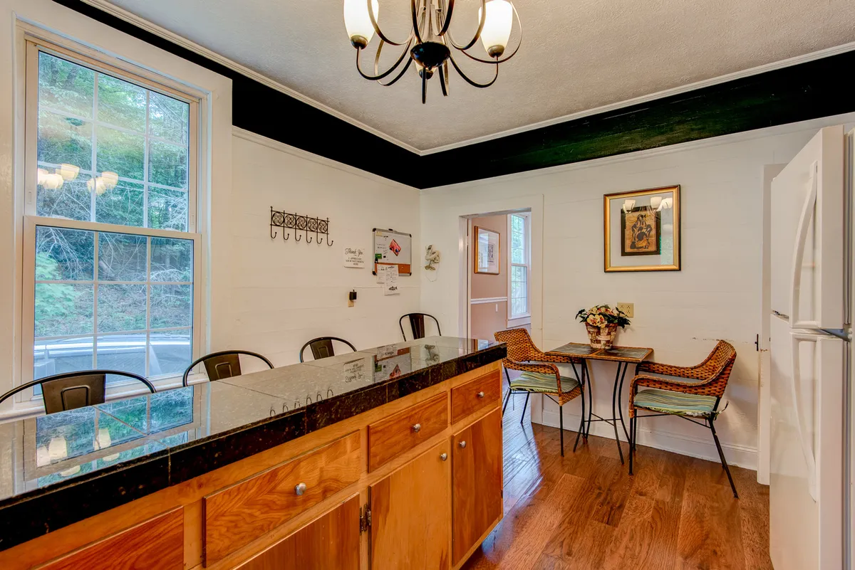 A kitchen and adjacent dining area where a black countertop island faces a sunlit window and a cozy dining table with chairs. The warm light, inviting layout, and harmonious design create a seamless flow between cooking and casual dining.