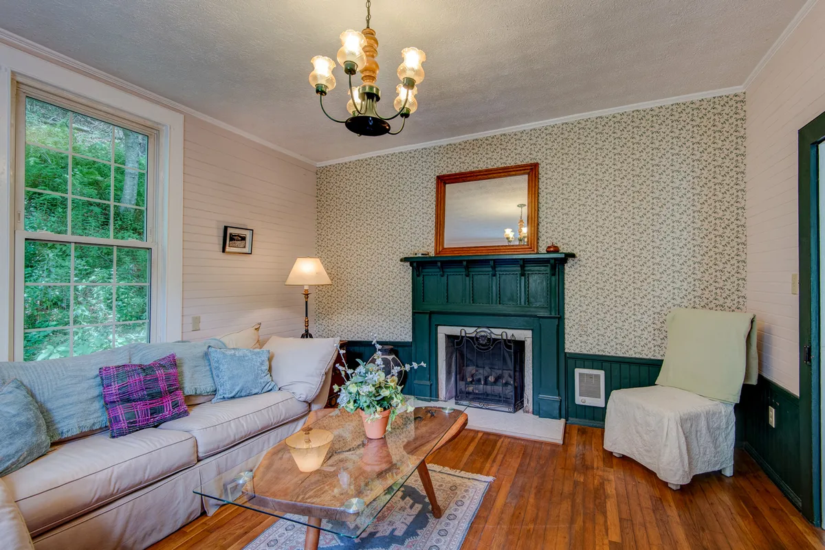 An inviting living area featuring a sofa, fireplace, chandelier, coffee table, and tasteful wall decor. The ambiance is warm and encourages both socializing and quiet reflection.