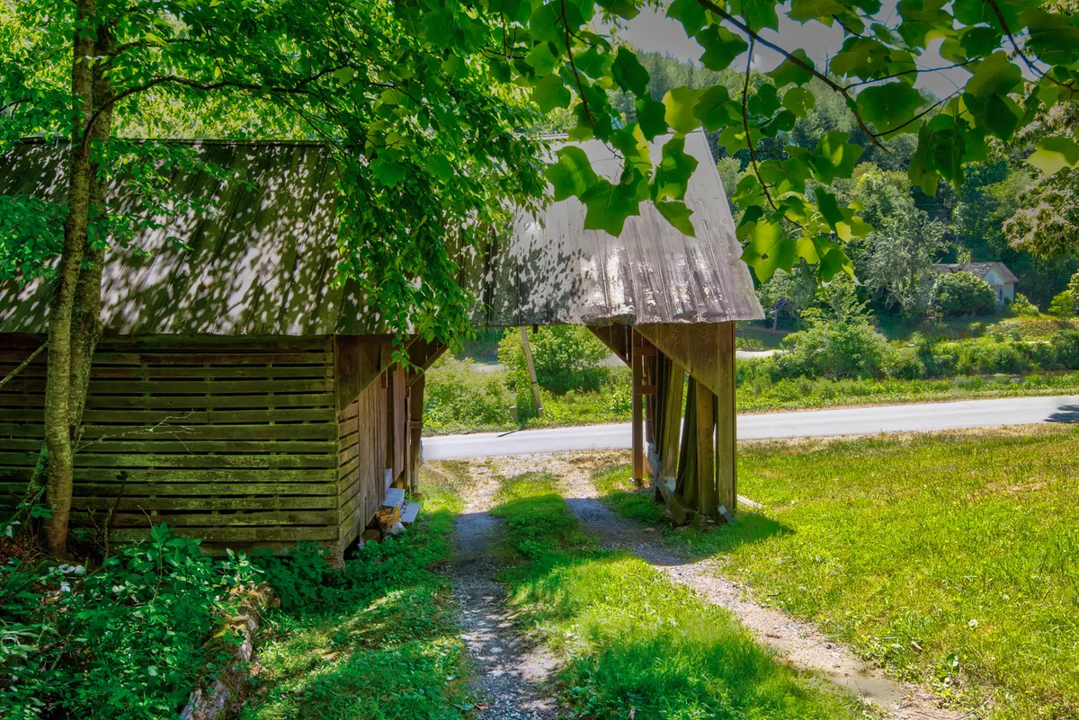 The photo captures rustic wooden structures nestled among lush greenery along a peaceful gravel path. The natural, tranquil setting is perfect for walking and enjoying the quiet beauty of the mountains.